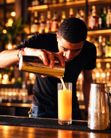 A bartender pouring a fresh cocktail from a shaker into a glass at the bar